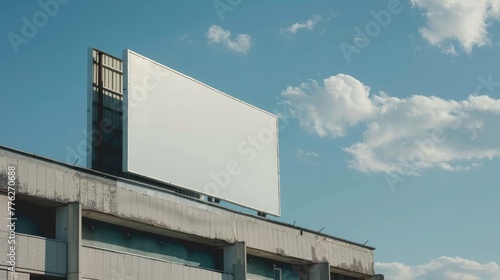 A large blank billboard ready for branding, placed on a modern office building against a backdrop of a sunny sky with fluffy clouds, evoking potential and opportunity. Street mockup, advertising