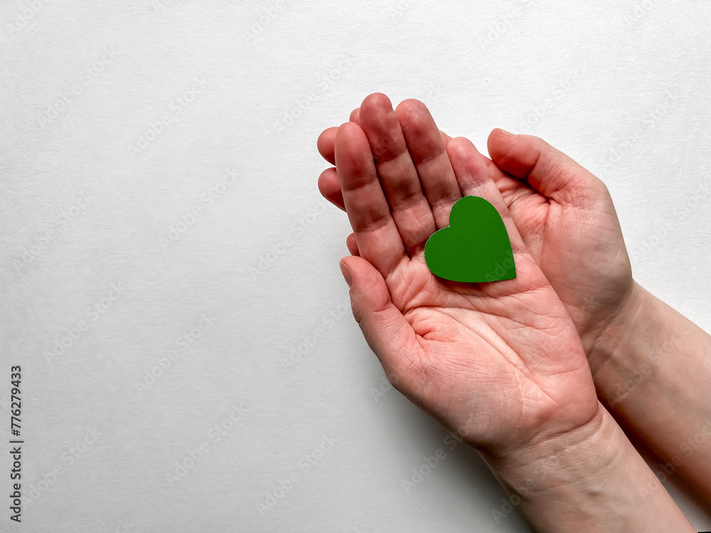 Female hands holding a green paper heart on a white background, Earth Day, April 22. Female hands holding a green paper heart on a white background, Earth Day, April 22.