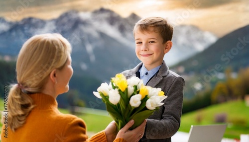 A boy giving a bouquet of fresh, beautiful flowers to his mother against the background of mountains and the setting sun