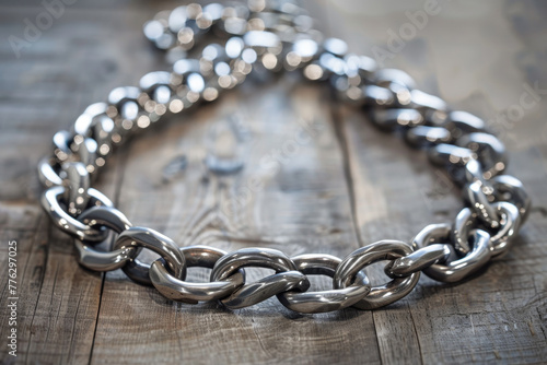 A silver chain with a silver clasp is laying on a wooden surface