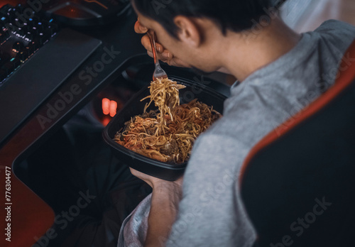 Young caucasian guy gamer eats wok food with a fork from a black container photo