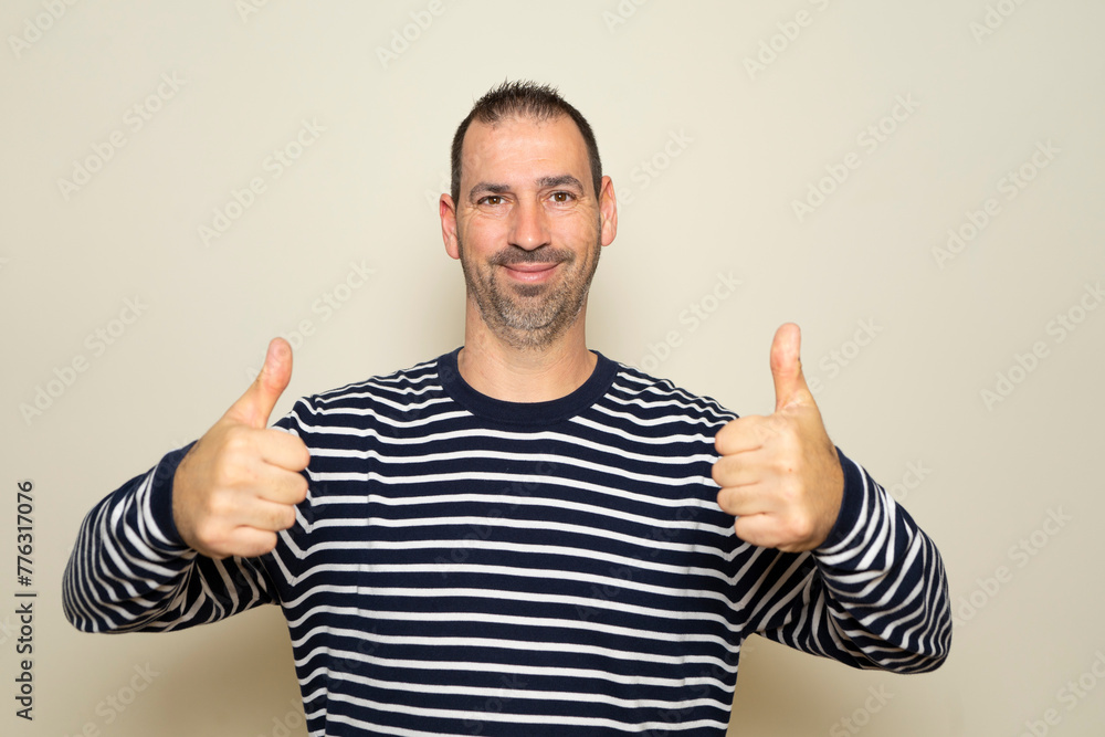 Bearded Hispanic man in his 40s wearing a striped sweater with thumbs up giving thumbs up to seaweed, isolated on beige studio background. Bearded Hispanic man in his 40s wearing a striped sweater with thumbs up giving thumbs up to seaweed, isolated on beige studio background.
