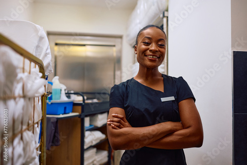 Black confident hotel housekeeper with her arms crossed looking at camera.