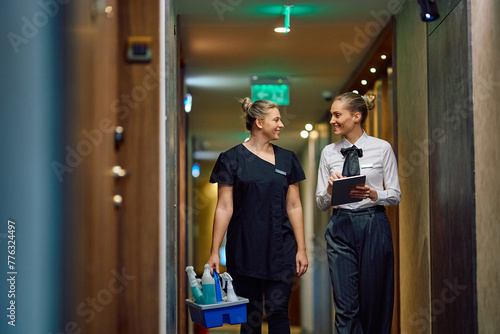 Happy hotel maid talking to housekeeping manager while waking through hallway, photo