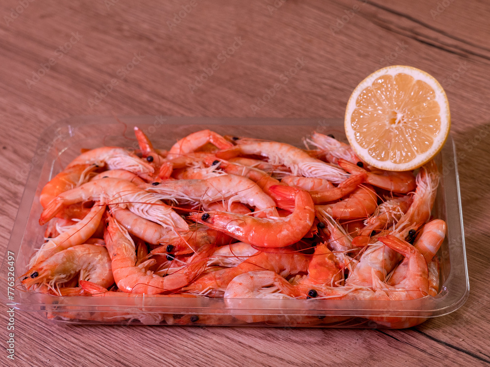 unpeeled shrimp in plastic with lemon, photo from the side, wood background unpeeled shrimp in plastic with lemon, photo from the side, wood background