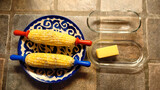 hot buttered sweet corn on the cob with sea salt and black pepper. Clear glass butter dish with butter also pictured. 