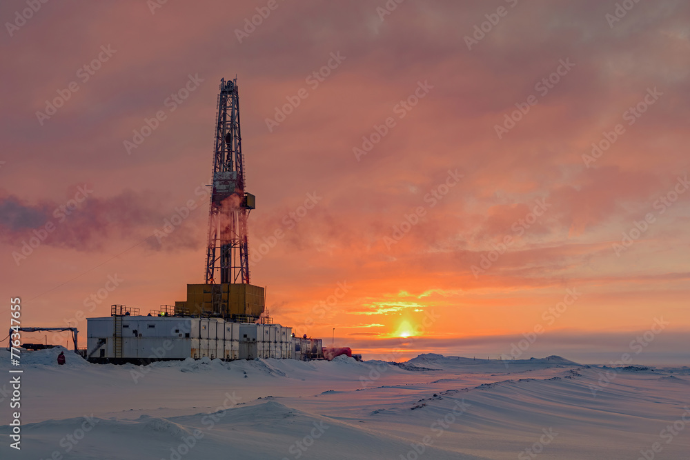 Drilling wells in an Arctic oil and gas field. Polar day sunrise in the background. Winter northern landscape against the beautiful sky