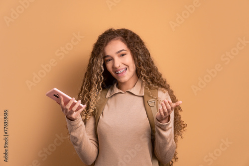 joyful female student smiling and holding mobile phone in beige colors. going to school, education, student concept.