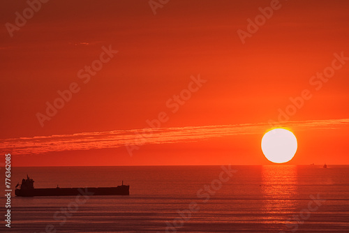 Fototapeta Naklejka Na Ścianę i Meble -  Sunset from Punta Galea, Getxo over the Cantabrian Sea with a round sun touching the horizon, a boat anchored in the sea and an intense orange sky