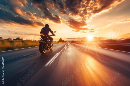 A motorcyclist rides on a highway towards the sunset, with the dynamic landscape blurring past photo