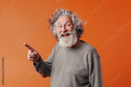 Joyful old man with curly hair pointing finger isolated on color background