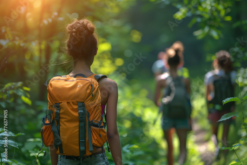 A group of hikers with backpacks walk in single file along a narrow forest trail, basked in the dappled sunlight filtering through the trees.Outdoor adventure and exploration in nature