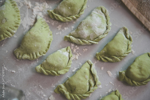 Close-up dumplings of green color on a floured table background. Traditional cuisine in Ukraine - varennyky with mashed potatoes and spinach