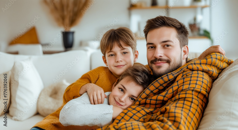 Man and two children wrapped in blanket on couch in living room. Man and two children wrapped in blanket on couch in living room.