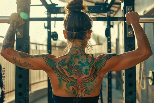 A woman with a tattoo of a bird on her back is lifting weights