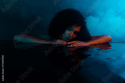 Passionate charming lady touching water relaxing in spa center mysterious atmosphere in dark illuminated bathroom