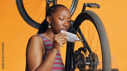 Knowledgeable repairman using specialized glue to recondition broken bicycle chain, orange studio background. Cyclist hobbyist applying adhesive on bike parts during inspection process