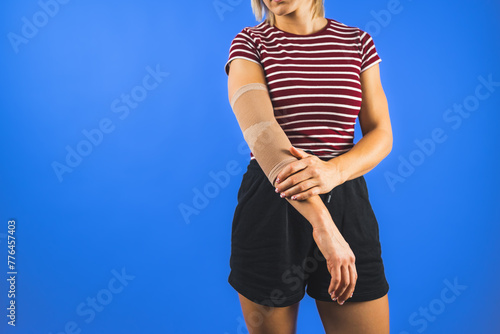a young woman wearing an elbow support brace over a blue background, trauma concept. High quality photo
