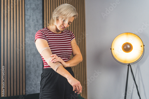 blond woman adjusting her elbow support brace at home, self-treatment concept. High quality photo