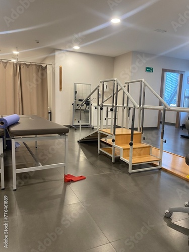 A well-equipped physical therapy room with various rehabilitation equipment, including parallel bars and therapy mats. 