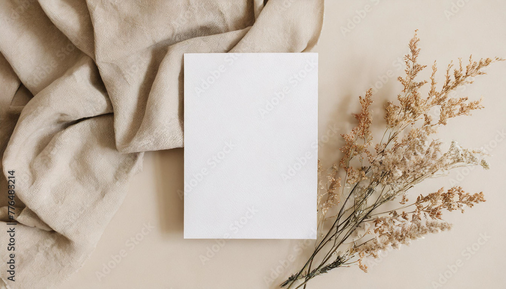 Blank paper sheet card with mockup copy space and dry floral branch and blanket cloth on neutral beige background. Minimal aesthetic wedding invitation template. Flat lay, top view Blank paper sheet card with mockup copy space and dry floral branch and blanket cloth on neutral beige background. Minimal aesthetic wedding invitation template. Flat lay, top view