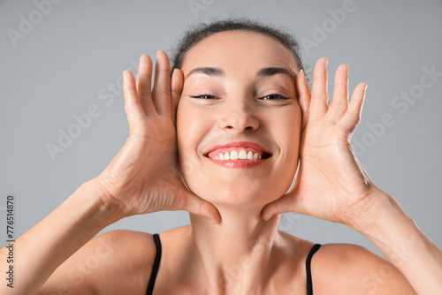 Beautiful mature woman giving herself face massage on grey background