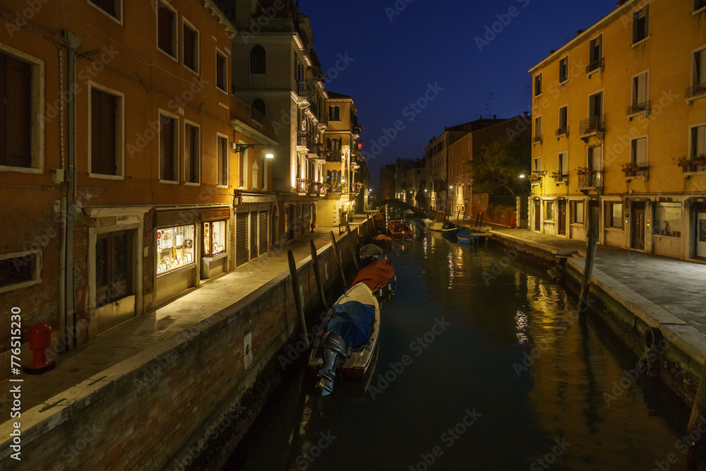 Typical townscape of a narrow canal surrounded by colorful building facades with boats during blue hour on a winter night, Venice, Veneto, Italy