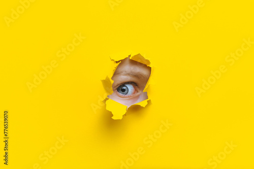 The right eye looks into a hole in the yellow paper. The child watches his parents. A curious look. Jealousy, eavesdropping concept. Copy space. photo