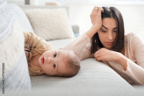 Little baby on sofa and young woman suffering from postnatal depression at home, closeup