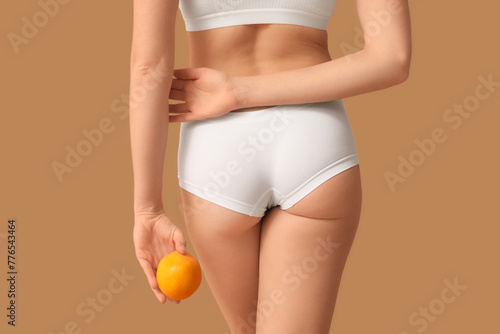 Beautiful young woman with cellulite problem and orange on brown background, back view