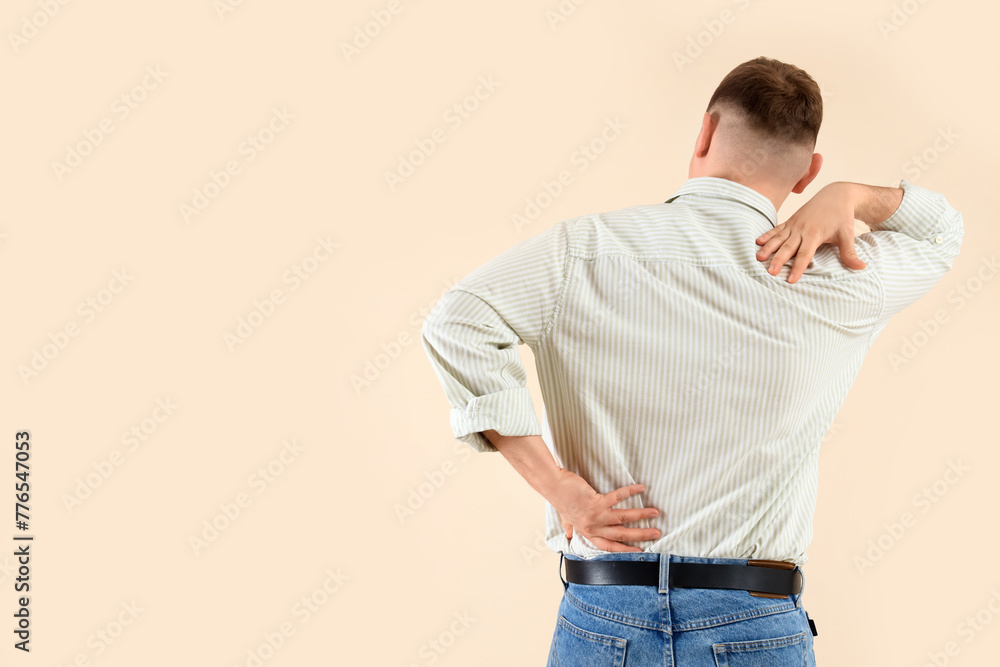 Young man suffering from back pain on beige background Young man suffering from back pain on beige background