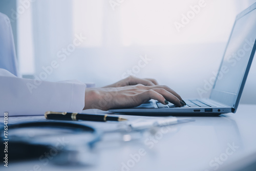 Doctor and patient sitting at the desk in clinic office. The focus is on female physician's hands filling up the medication history record form, close up. Medicine concept