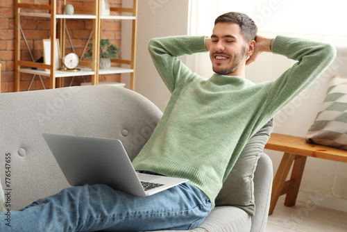 Handsome young happy man with laptop resting on sofa at home #776547655