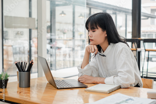 Attentive woman is engrossed in her laptop at a sunlit cafe table, a picture of concentration and calm productivity.