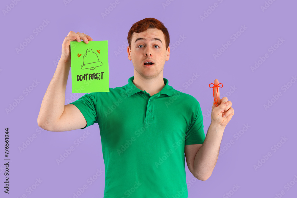 Young man holding paper with text DON'T FORGET and red bow on his finger against lilac background Young man holding paper with text DON'T FORGET and red bow on his finger against lilac background