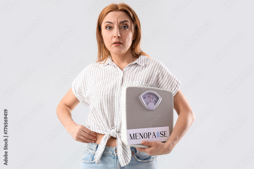 Mature woman holding paper with word MENOPAUSE and weight scales on light background - obrazy, fototapety, plakaty 