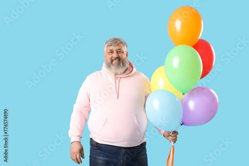 Senior man with bunch of colorful balloons on blue background © Pixel-Shot