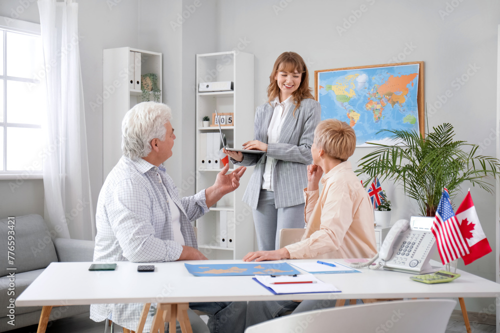 Female travel agent with laptop and mature couple in office Female travel agent with laptop and mature couple in office