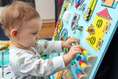Baby plays with wooden elements on a busy board