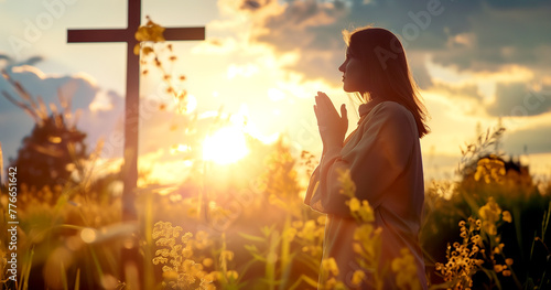 A woman is praying at the cross in the evening sunlight.