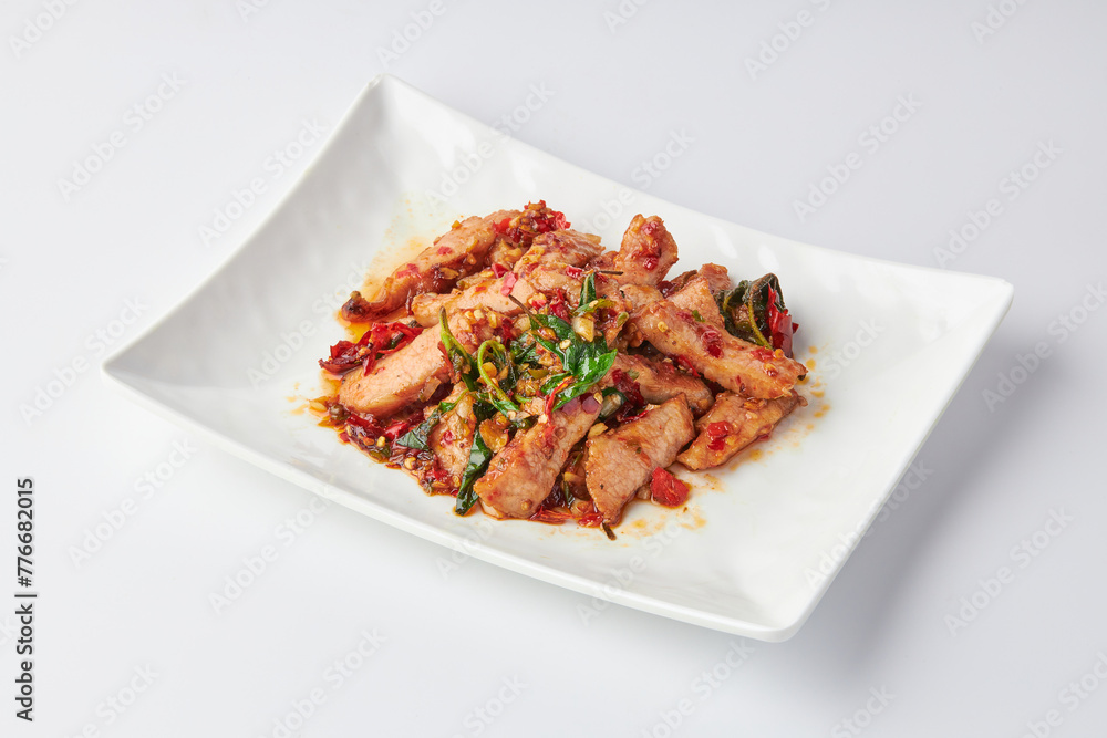 Thai spicy stir-fried grilled pork neck (Pork Jowl) with holy basil leaves served in white plate isolated on white background. Hot and spicy. Thai spicy stir-fried grilled pork neck (Pork Jowl) with holy basil leaves served in white plate isolated on white background. Hot and spicy.