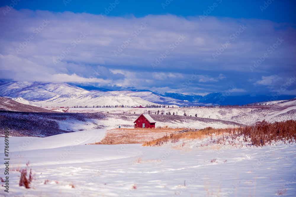 Red winter barn in the mountains of Colorado surrounded by the mountain peaks and snowy prairie Red winter barn in the mountains of Colorado surrounded by the mountain peaks and snowy prairie