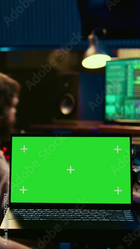 Vertical Video Audio technician leveling sound on recorder mixing console, having a laptop that shows greenscreen display. Producer turns up the volume of tracks in professional studio, control room