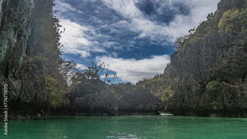 Picturesque karst limestone cliffs with steep slopes surround the bay. Highlights on the emerald water. Clouds in the blue sky. Small lagoon. Philippines. Palawan. El Nido