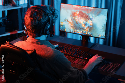 Host channel of young gaming streamer playing fighting Moba at battle arena game with multiplays team, wearing headphone on pc monitor with back side image at neon digital light modern room. Gusher. photo