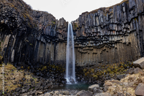 A majestic waterfall cascades over bedrock surrounded by rocks in the middle of a canyon, creating a stunning water feature in the natural landscape. Iceland