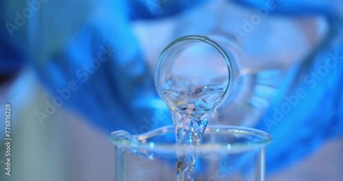 Clear liquid is poured from glass beaker into another glass beaker in laboratory photo