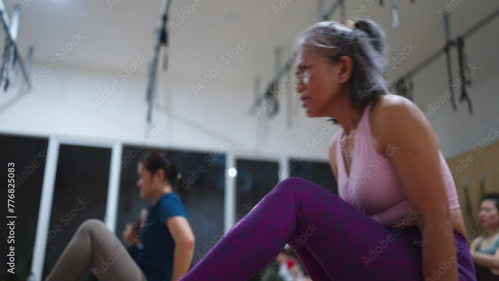 A woman in a pink tank top is sitting in a yoga class. The other women in the class are also wearing pink A woman in a pink tank top is sitting in a yoga class. The other women in the class are also wearing pink
