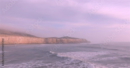 Sea waves, cliffs and lighthouse at sunset with foam near the shore. Sea surface aerial view of sea. Puerto Eten, Peru.