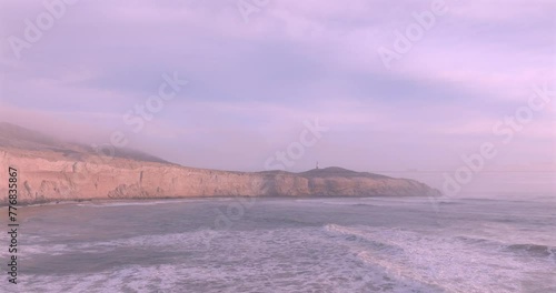 Sea waves, cliffs and lighthouse at sunset with foam near the shore. Sea surface aerial view of sea. Puerto Eten, Peru.